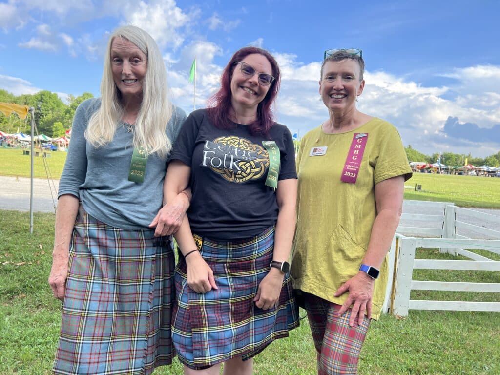 Three women wearing Scottish kilts and tartan pose together.